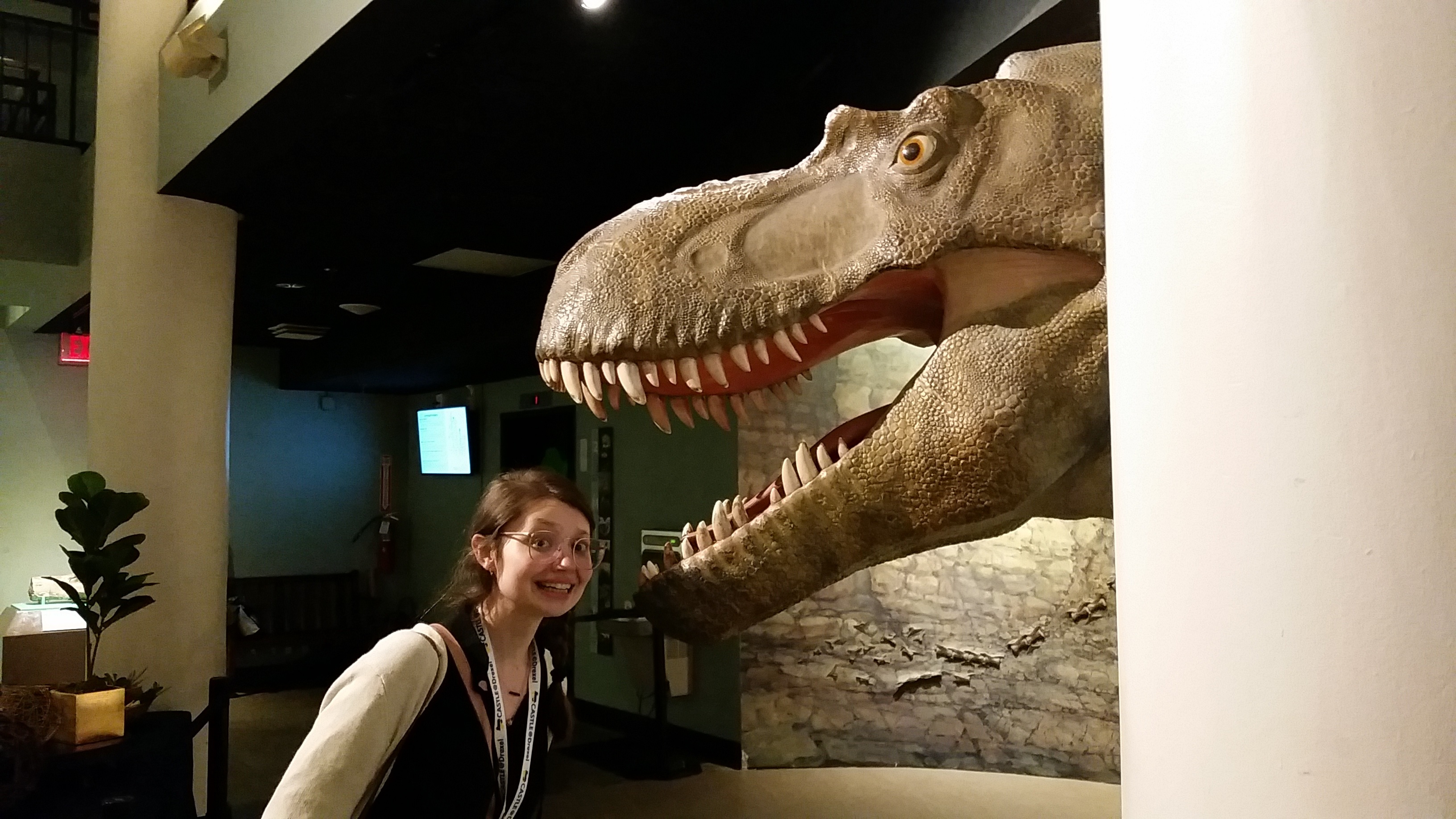 Cait standing beneath an open-mouth dinosaur model looking very scared.